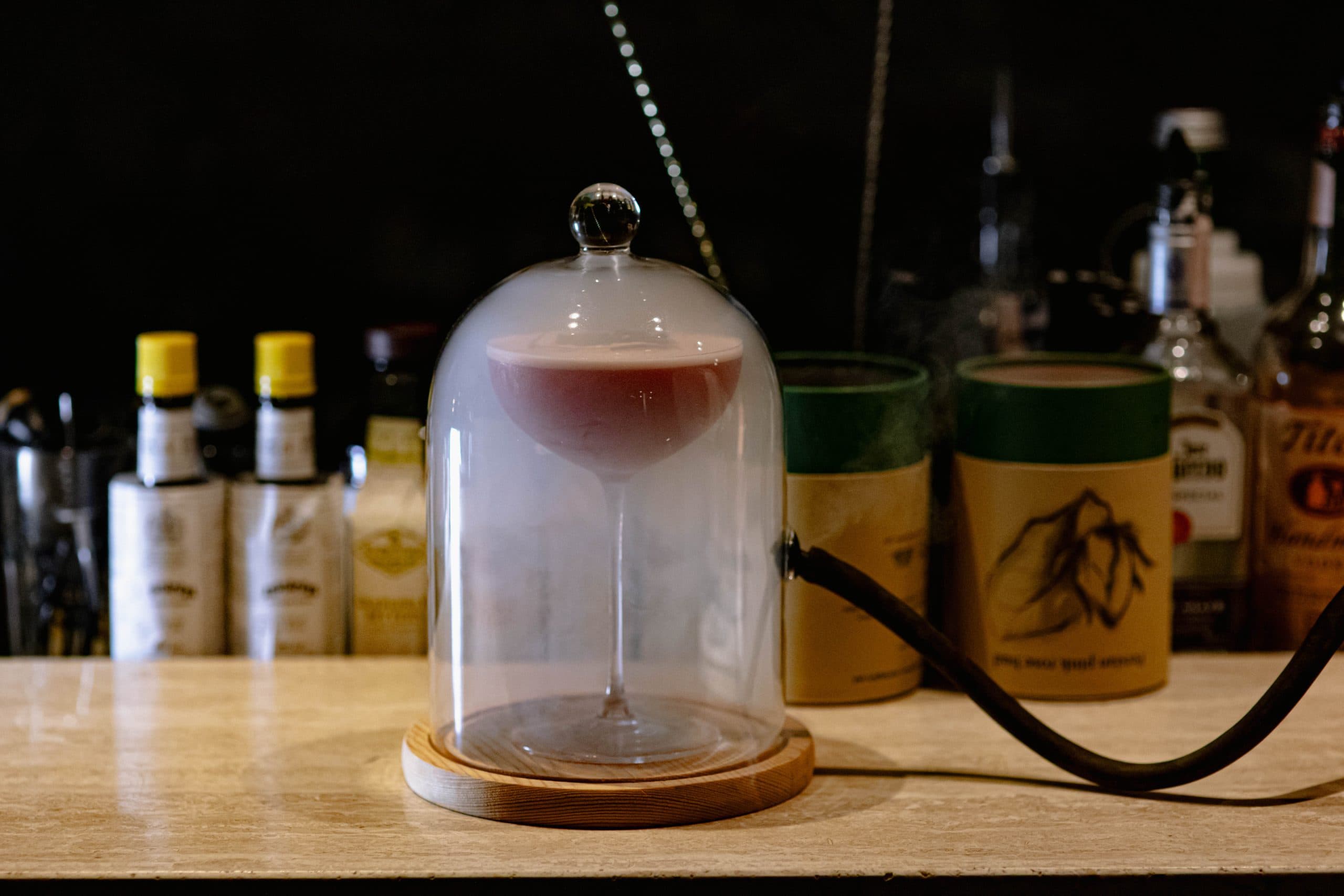 A smoked cocktail under a glass cloche at the bar