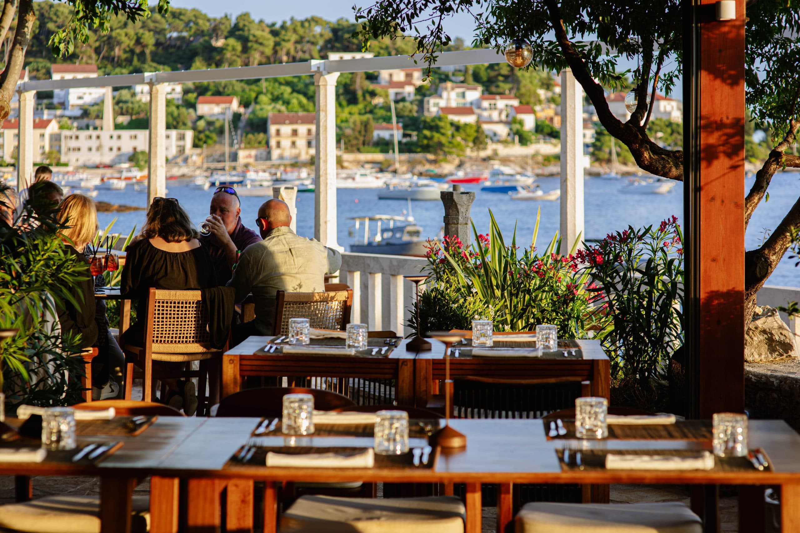 Guests dining on the terrace at golden hour, harbour behind